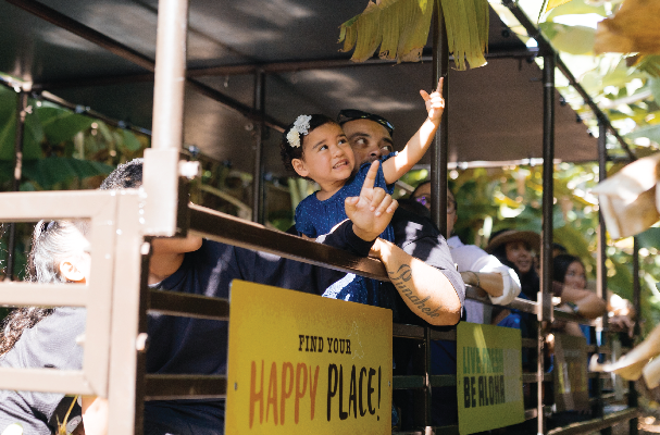 People on a vehicle with a 'Find Your Happy Place' sign, surrounded by greenery.